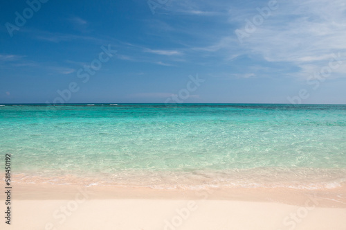 Deserted white sand beach with crystal clear sea against blue sky. Concept of escape, vacation & relaxation. Background image.