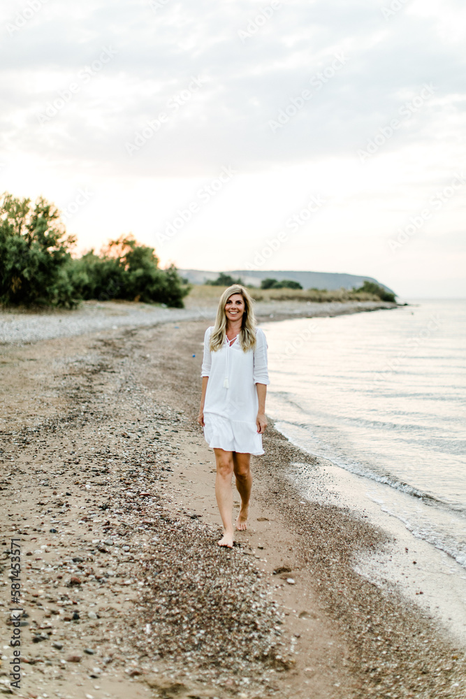 Frau im weißen kurzen Kleid geht am Strand entlang am Meer