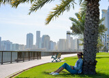 Happy tourist relaxing on lawn under palm tree in Sharjah while looking at camera. Vacation and sightseeing concept