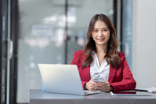 Beautiful Asian businesswoman using a smartphone to view social media applications, answer customer chats, transact through applications online job in an office.