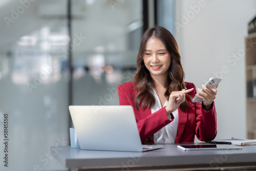 Beautiful Asian businesswoman using a smartphone to view social media applications, answer customer chats, transact through applications online job in an office.