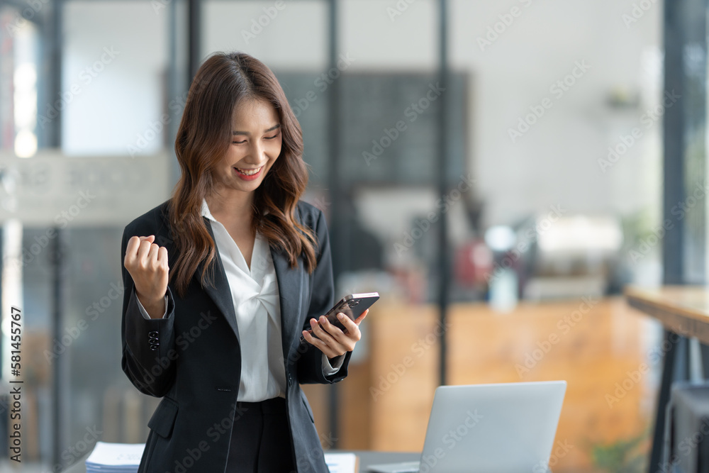 Asian businesswoman holding mobile phone with laptop looking at information laughing at news for online shopping happy. Asian businesswoman holding mobile phone with laptop looking at information laughing at news for online shopping happy.