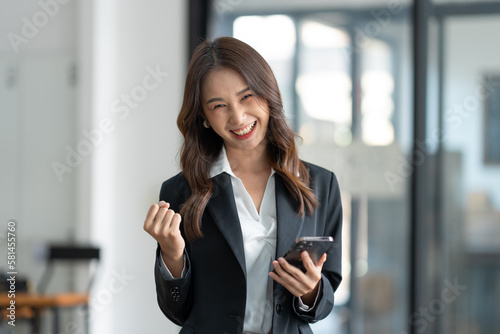 Asian businesswoman holding mobile phone with laptop looking at information laughing at news for online shopping happy.