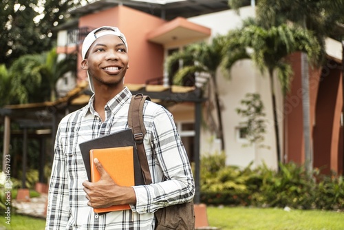 Confident student wearing a cap and holding books.