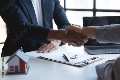 Two young Asian businessmen shake hands after signing a contract to invest in a village project. real estate  with businesswomen joining in showing joy and clapping in the office.