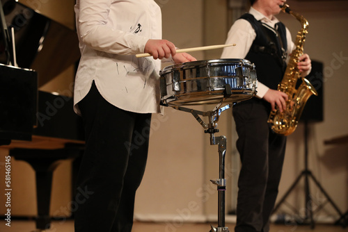 Young musicians play the drum and saxophone at a school concert standing on stage