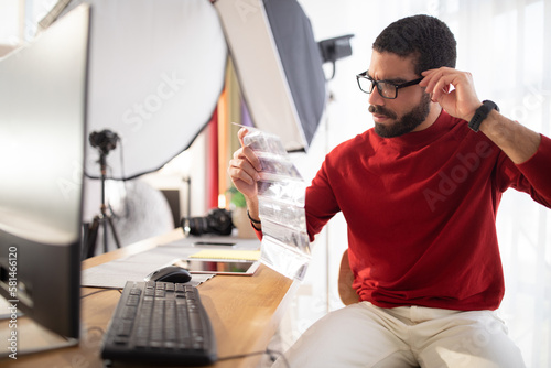Concentrated hispanic man photographer checking photographic flims at office