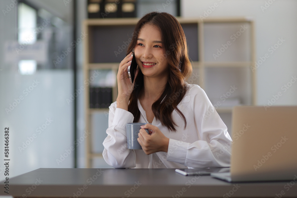 Beautiful Asian businesswoman talking on the phone with a customer while working at her desk in the office. Beautiful Asian businesswoman talking on the phone with a customer while working at her desk in the office.