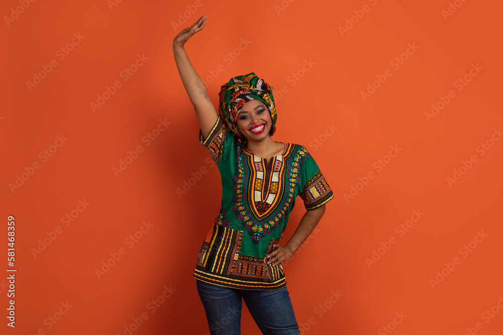 Positive funny black woman in african costume dancing on orange Positive funny black woman in african costume dancing on orange