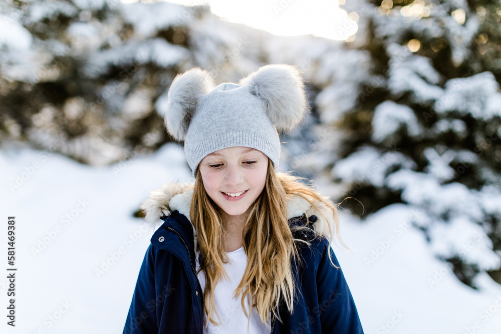 Glückliches lachendes hübsches Mädchen mit langen Haaren mit Bommelmütze im Wald im Winter mit Schnee Glückliches lachendes hübsches Mädchen mit langen Haaren mit Bommelmütze im Wald im Winter mit Schnee