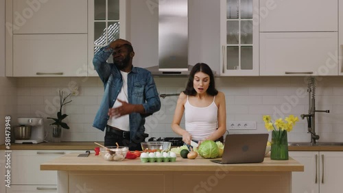 African american man and caucasian woman are making salad together in the kitchen at home. The couple is watching a sports game and cheering for their favorite team after they score a goal. photo