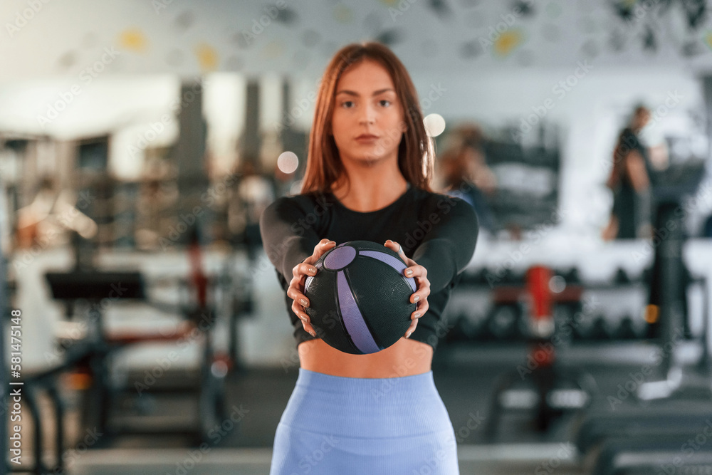Fitness ball in hands. Standing and posing. Beautiful woman with sport body type is in the gym