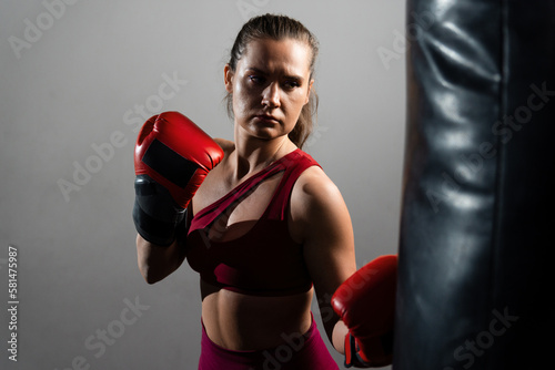 A boxer woman in a red tracksuit hits a punching bag