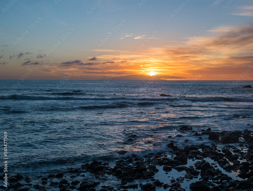Pink orange golden sunset with waves at a black sand beach with lava stones and rock, Sun setting to the atlantic ocean. La gomera island, Canary Islands
