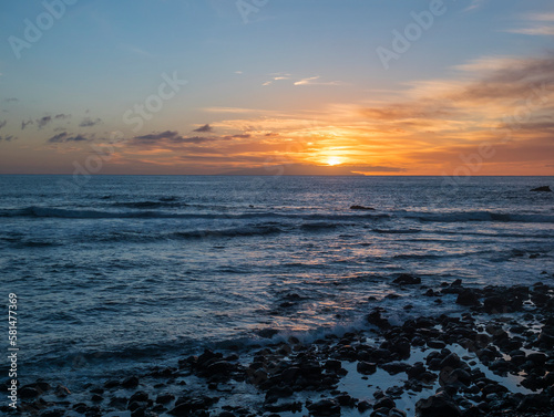Pink orange golden sunset with waves at a black sand beach with lava stones and rock, Sun setting to the atlantic ocean. La gomera island, Canary Islands