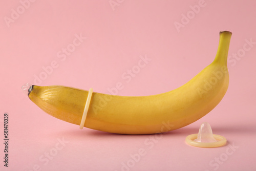 Condom and banana on pink background with copy space