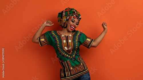 Joyful pretty black woman in african costume dancing on orange