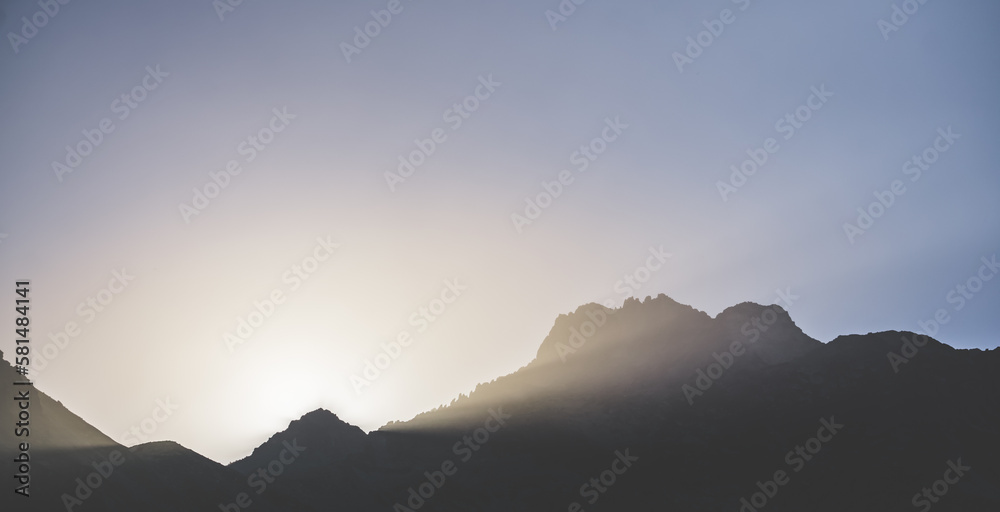 Minimalistic mountain landscape, the sun's rays shine from behind the mountain, a dark mountain at sunset in the evening, a panorama of minimalism in the mountains