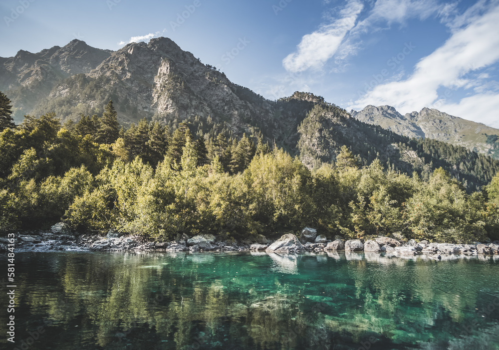Mountain landscape with a cold mountain lake against the backdrop of a forest and a rocky peak in the mountains, a mountain reflection in the lake, a landscape in the mountains in a warm sunny summer