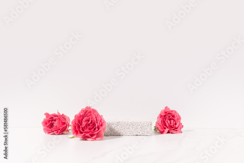Beauty cosmetics product presentation scene made with pumice stone pedestal and pink roses on white table. Studio photography.