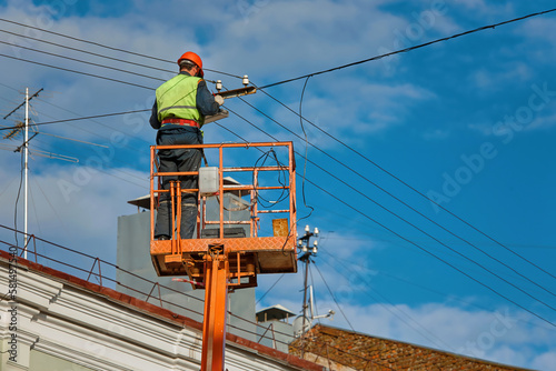 Worker on cherry picker install led lantern on electric wires at height on city street. Man in lift bucket upgrade street lights, install led panel. Improving outdoor lights on energy efficient light