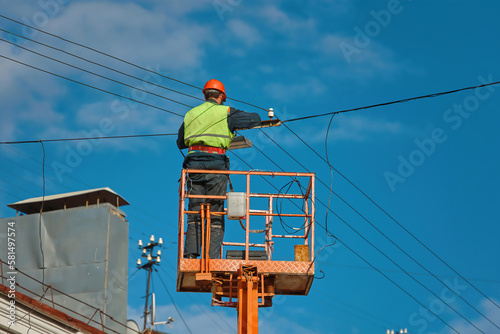 Worker in lifting cradle install led lantern on electric wires at height on city street. Man in lift bucket upgrade street lights, install led panel. Improving outdoor lights on energy efficient light