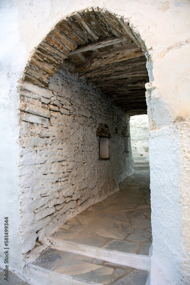Tinos island, Dio Horia village Cyclades Greece. Arched wall covers narrow paved corridor. Vertical