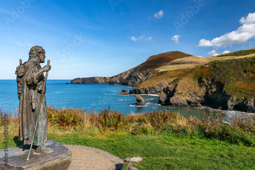 The statue of Saint Carannog keeps watch over the bay at Llangrannog, with Carreg Bica ( Bica's Tooth) and the headland of Ynys Lochtyn in the background.