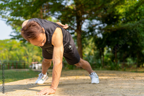 sporty handsome Asian man doing one arm push up bodyweight exercise in city public park on summer day, strong young guy full of energy workout outdoors for healthy and active lifestyle