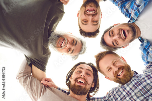 Team of men huddling. Group of male friends hugging. Bottom view of five happy young and mature bearded men standing head to head in circle, looking down at camera, smiling, laughing, and having fun © Studio Romantic