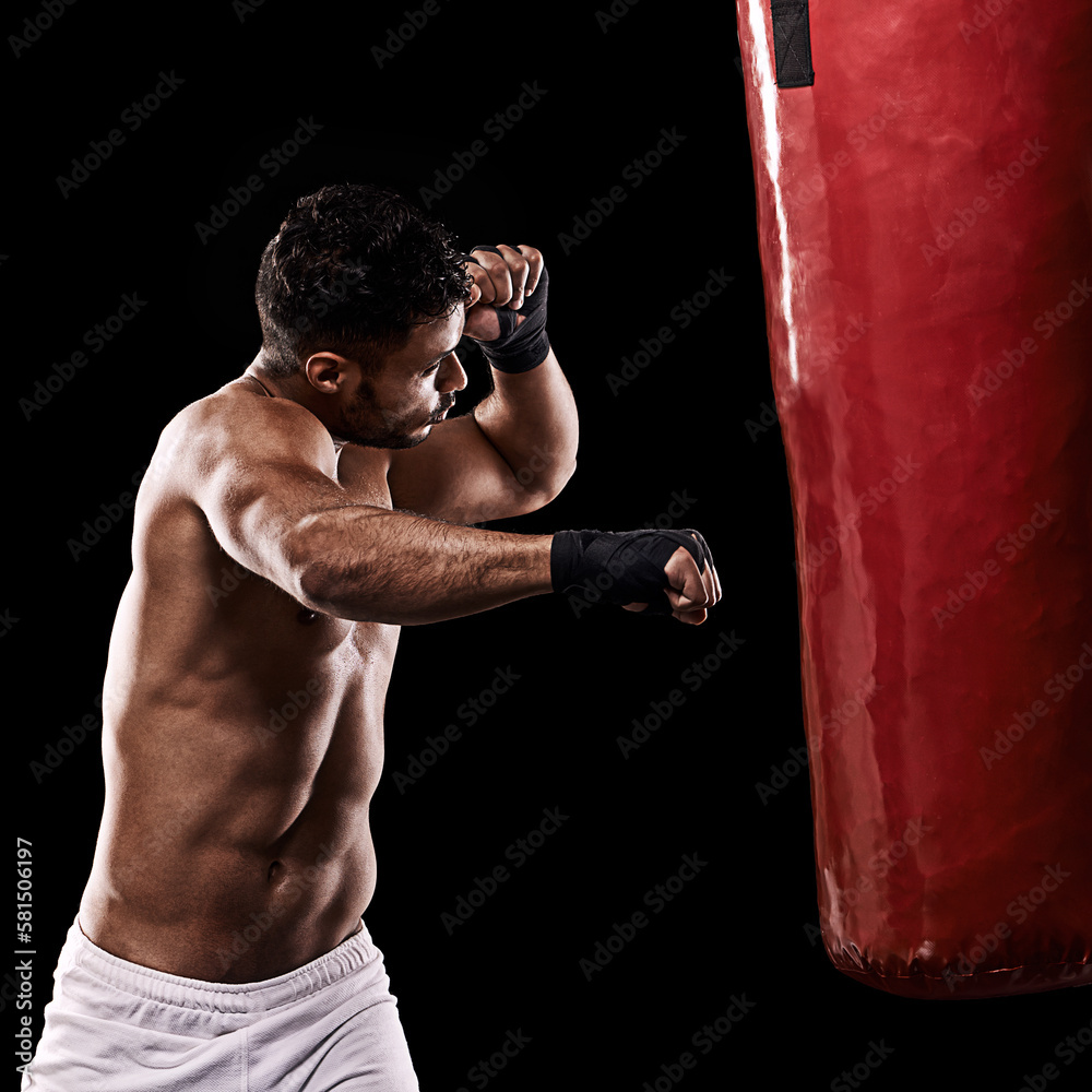 Delivering a powerful right hook. Studio shot of kick boxer working out with a punching bag against a black background. Delivering a powerful right hook. Studio shot of kick boxer working out with a punching bag against a black background.