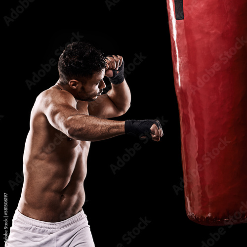 Delivering a powerful right hook. Studio shot of kick boxer working out with a punching bag against a black background.