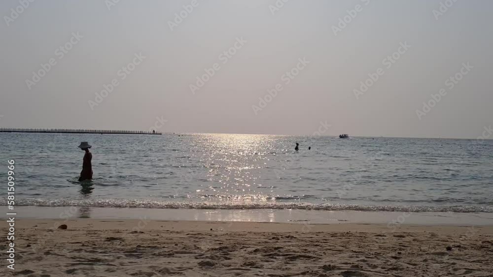 Silhouette of woman wearing bikini and hat walking on the sandy beach during golden sky sunset. People enjoying ocean waves on summer vacation or beach trip. Holidays on tropical seaside high season. Silhouette of woman wearing bikini and hat walking on the sandy beach during golden sky sunset. People enjoying ocean waves on summer vacation or beach trip. Holidays on tropical seaside high season.