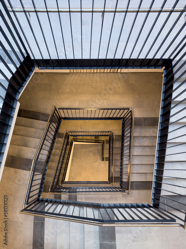 Bird's-eye view from top to bottom of stairwell in tall block of flats with banisters with black poles © A2LE