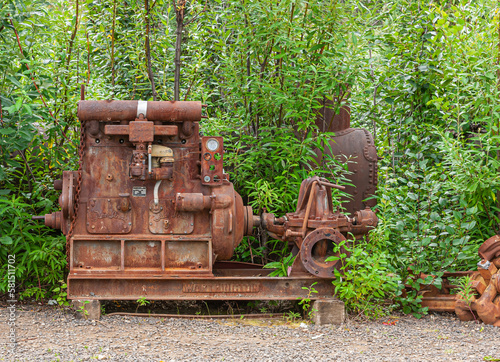 Fox, Alaska, USA - July 26, 2011: Eldorado Gold Mine museum and park. Old rusted-metal, heavy steam disperser machine as used in placer mining set against green tree backdrop