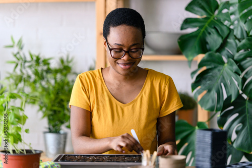 Young smiling african-american woman doing seed-starting early in the spring indoors for her backyard garden or a homestead garden