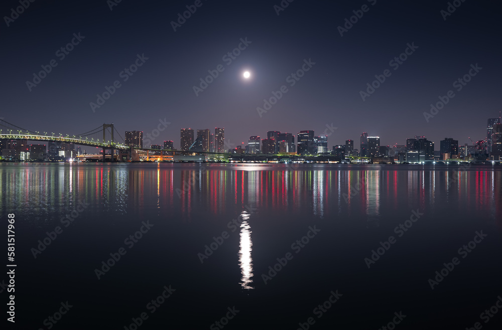Tokyo skyline under full moon. Night photo with the modern skyscraper office buildings in Tokyo and Rainbow Bridge.
