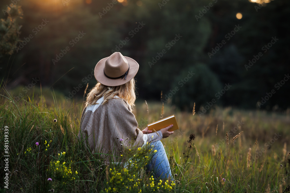 Woman is relaxing in nature and reading a book to improve her mindfulness and mental health - obrazy, fototapety, plakaty 