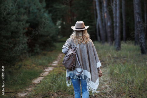 Woman with poncho  cowboy hat and backpack walking in forest