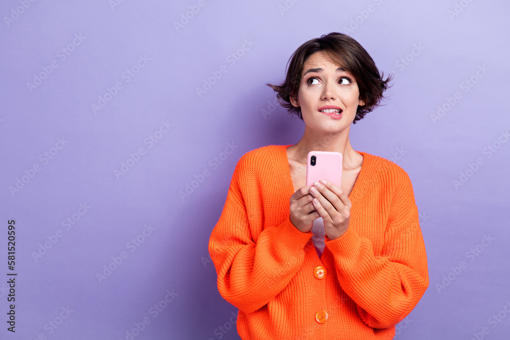 Photo of nervous uncertain lady dressed orange cardigan chatting device looking empty space isolated purple color background - obrazy, fototapety, plakaty 