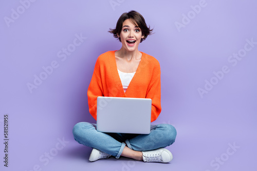 Full body length photo of funny surprised funny girl wear orange stylish pullover watch youtube video netbook isolated on violet color background
