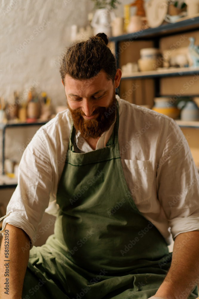 Fototapeta premium Pottery workshop satisfied and smiling bearded potter at work