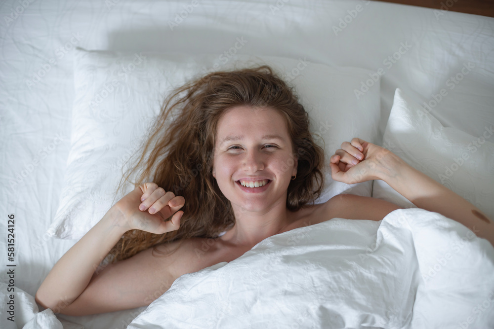 Young happy beautiful sleepy woman in the bed in bedroom at home in the morning lying under white blanket, enjoy resting, sleep well, wake up and smile. Good morning Young happy beautiful sleepy woman in the bed in bedroom at home in the morning lying under white blanket, enjoy resting, sleep well, wake up and smile. Good morning