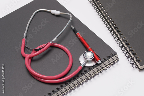Stetoskop lekarski ułożony na notatniku z długopisem na białym tle