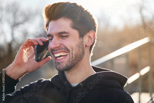 Close up of laughing hispanic man talking on the phone outside during sunset. With a beautiful smile.