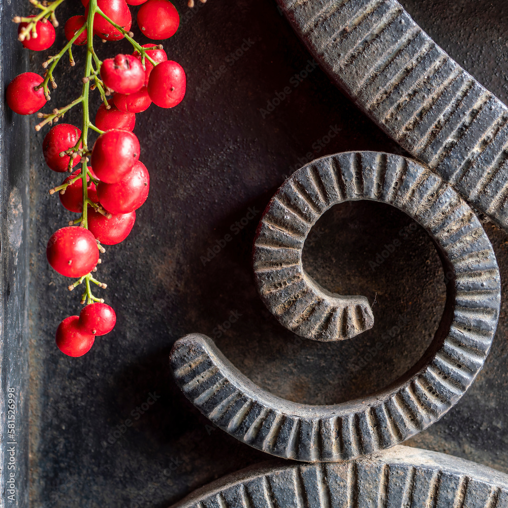 Black, rough forged iron surface with curved shaped decor and a bunch of bright red peppercorn fruits. Black, rough forged iron surface with curved shaped decor and a bunch of bright red peppercorn fruits.