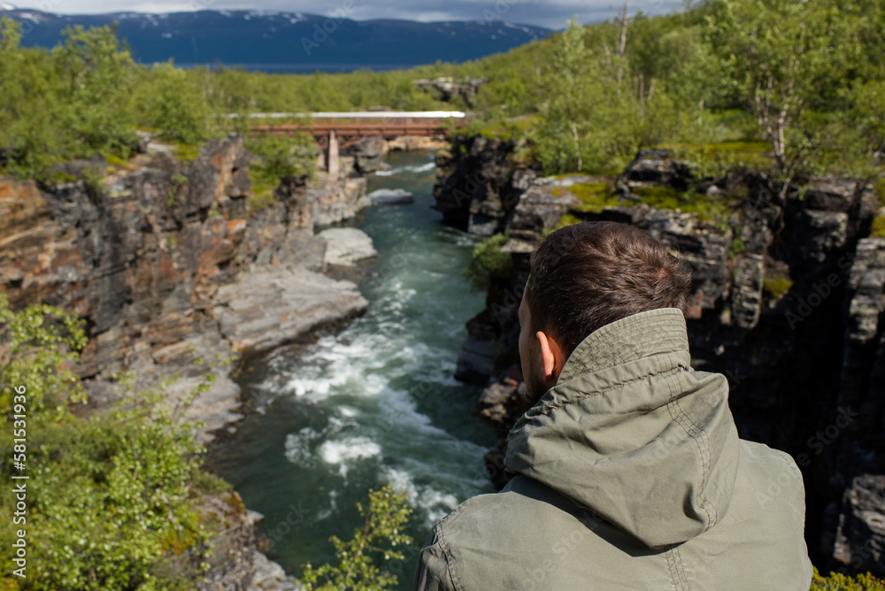 Naklejka premium A man is enjoying the beautiful natural scenery in the north. Canyon and mountain river. Tourist attraction in Finland. Amazing scenic outdoor view. Travel, adventure, relaxed lifestyle