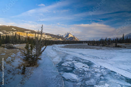 frozen siffleur mountain river during sunrise with pieces of ice in water and mountains on background