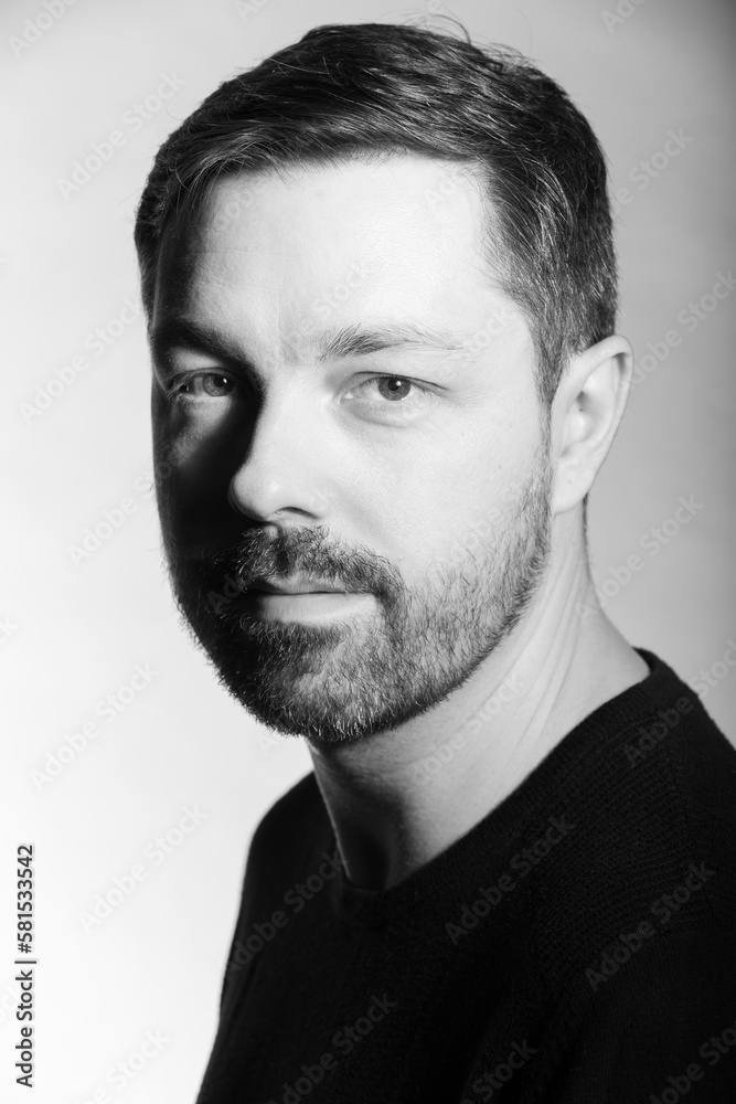 Fototapeta premium Black and white studio portrait of a 40 year old caucasian male. Men's fashion photoshoot. He has a beard and dark hair. 
