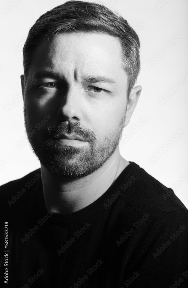 Fototapeta premium Black and white studio portrait of a 40 year old caucasian male. Men's fashion photoshoot. He has a beard and dark hair. 